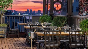 Un espace de restauration en plein air avec des tables et des chaises, une vue sur les toits de la ville et un mur décoratif orné d’un motif circulaire.