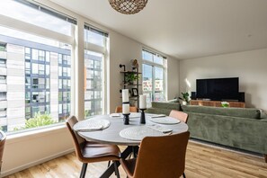Uma sala de estar moderna com área de jantar, janelas amplas, TV de tela plana e sofá verde.