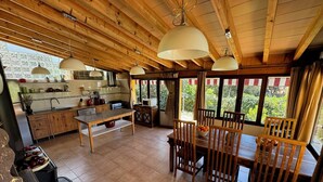 A rustic kitchen with wooden beams, a dining area with a table and chairs, and large windows offering a view of greenery. - Tranquil Mallorca Villa Seaside Getaway with Pool (IB)