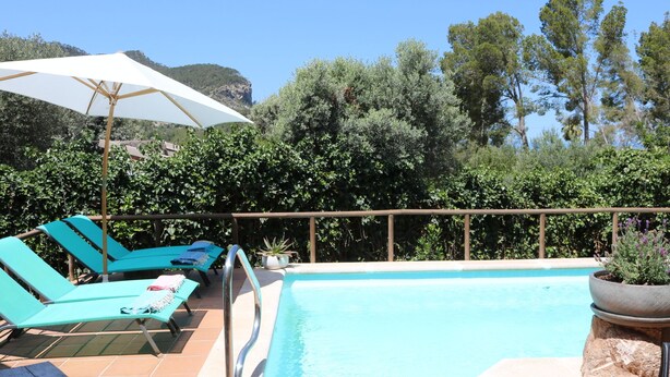A swimming pool with lounge chairs and umbrellas, surrounded by greenery and a mountainous backdrop. - Tranquil Mallorca Villa Seaside Getaway with Pool (IB)