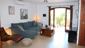 A living room with a blue sofa, a brown leather chair, a wooden coffee table, and a lamp. There is a door leading to a balcony with a view of greenery. - Tranquil Mallorca Villa Seaside Getaway with Pool (IB)