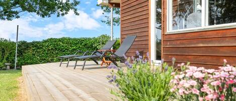 Een houten terras met ligstoelen en een bloeiende plant in een pot.