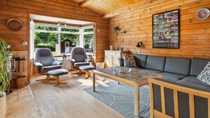 A cozy cabin interior with wooden walls, a sofa, two armchairs, a dining table, and a large window offering a view of the outdoors. - "Swipdagh" - 150m from the sea by Interhome (Martofte)