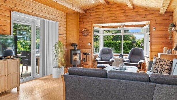 A cozy cabin interior with a sofa, chairs, a TV, a fireplace, and a large window offering a view of greenery. - "Swipdagh" - 150m from the sea by Interhome (Martofte)