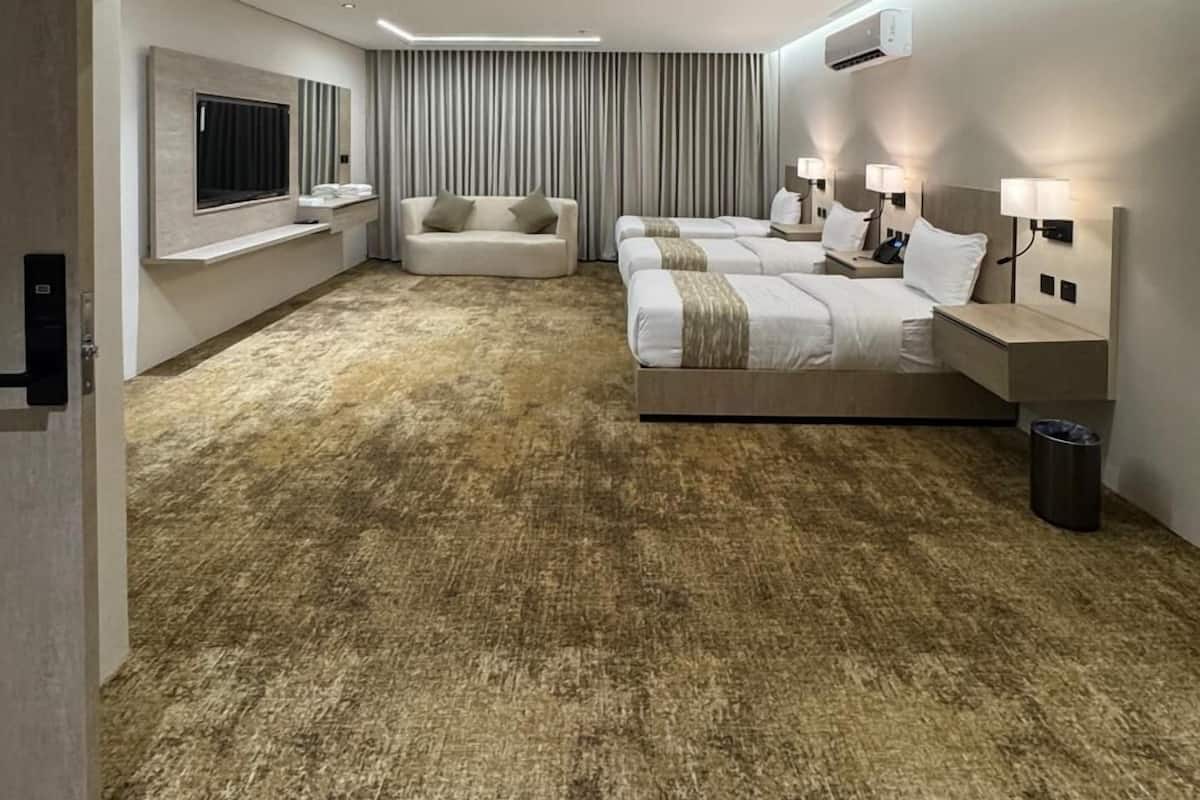 A modern hotel room with a large bed, a sofa, a TV, and a minibar.