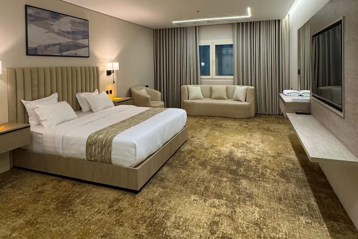 A modern hotel room with a large bed, a sofa, a TV, and a window with curtains.