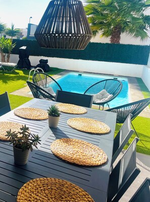 Une terrasse extérieure avec une piscine, des sièges et une table agrémentée de sets de table en fibres tressées et de plantes en pot.