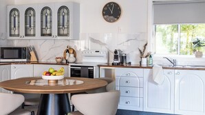 Una cocina moderna con armarios blancos, una mesa redonda de madera y un reloj en la pared.