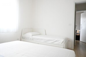 A single bed with a white headboard in a room with white walls and a door leading to another room.