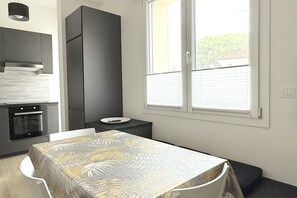 Cocina compacta con electrodomésticos modernos, comedor con mantel estampado y ventana con persianas.