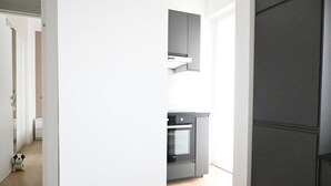 Une cuisine moderne dotée d’un four encastré et de placards, un couloir avec un jouet en peluche, et une porte donnant sur une autre pièce.