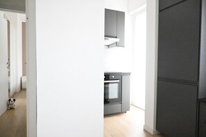 Eine moderne Küche mit Einbauofen und Schränken, ein Flur mit einem Kuscheltier und eine Tür zu einem weiteren Raum.