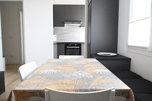 A modern kitchen with dark cabinets, a built-in oven, and a dining area with a table and chairs.