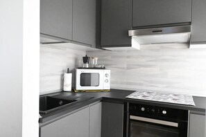 A modern kitchen with grey cabinetry, a built-in microwave, and a stainless steel range hood.