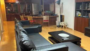 Un salon moderne avec un canapé en cuir noir, une petite table basse et un coin repas comprenant des chaises en bois, avec une cuisine en arrière-plan.