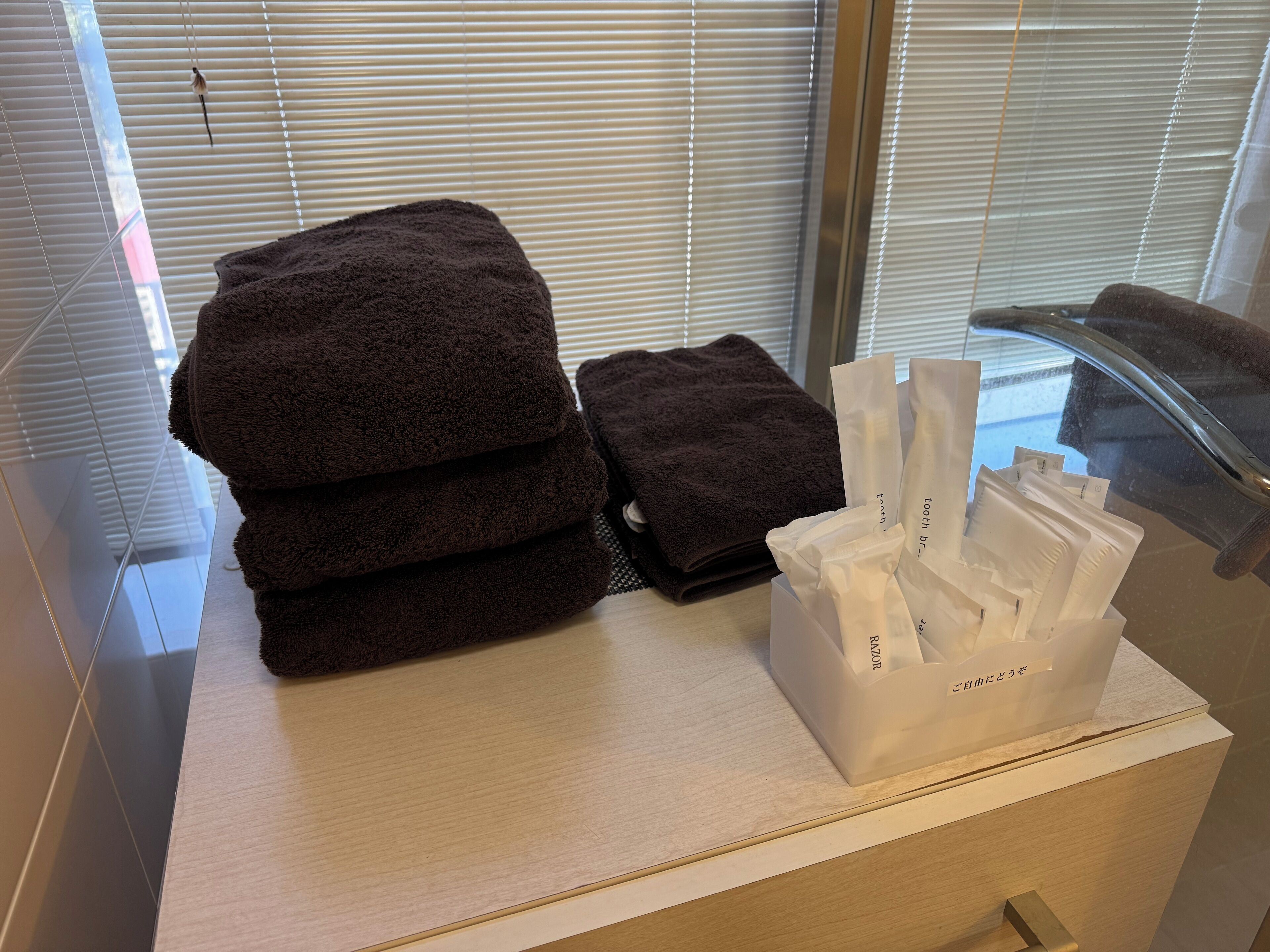 A bathroom with a stack of dark towels, a white tissue box, and a glass shower enclosure.