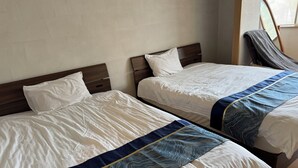 Deux lits avec des draps blancs et des bordures décoratives bleues, des têtes de lit en bois et une fenêtre donnant sur un paysage verdoyant.