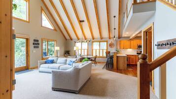 A spacious living area with a high ceiling and wooden beams, a dining area with a view, and a kitchen with wooden cabinets.