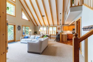 A spacious living area with a high ceiling and wooden beams, a dining area with a view, and a kitchen with wooden cabinets.