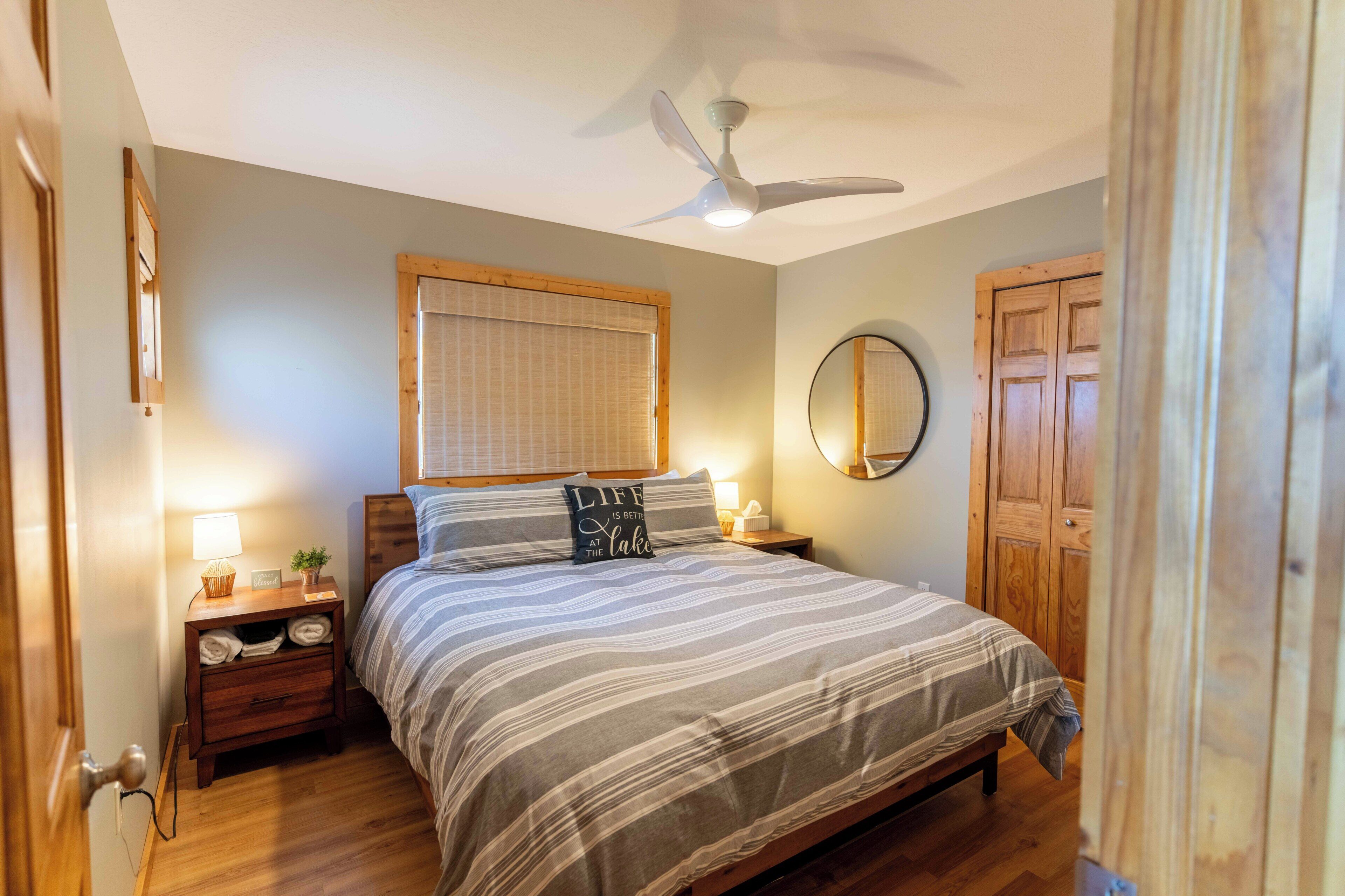 Un dormitorio con cama, mesitas de noche, ventilador de techo, espejo y puerta de madera.