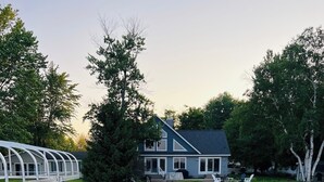 Een houten steiger die naar een huis aan een meer leidt, met een overdekte doorgang aan de linkerkant.