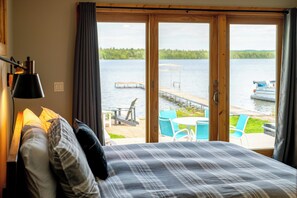 Een slaapkamer met een bed, een lamp en uitzicht op een meer met stoelen en een aanlegsteiger.