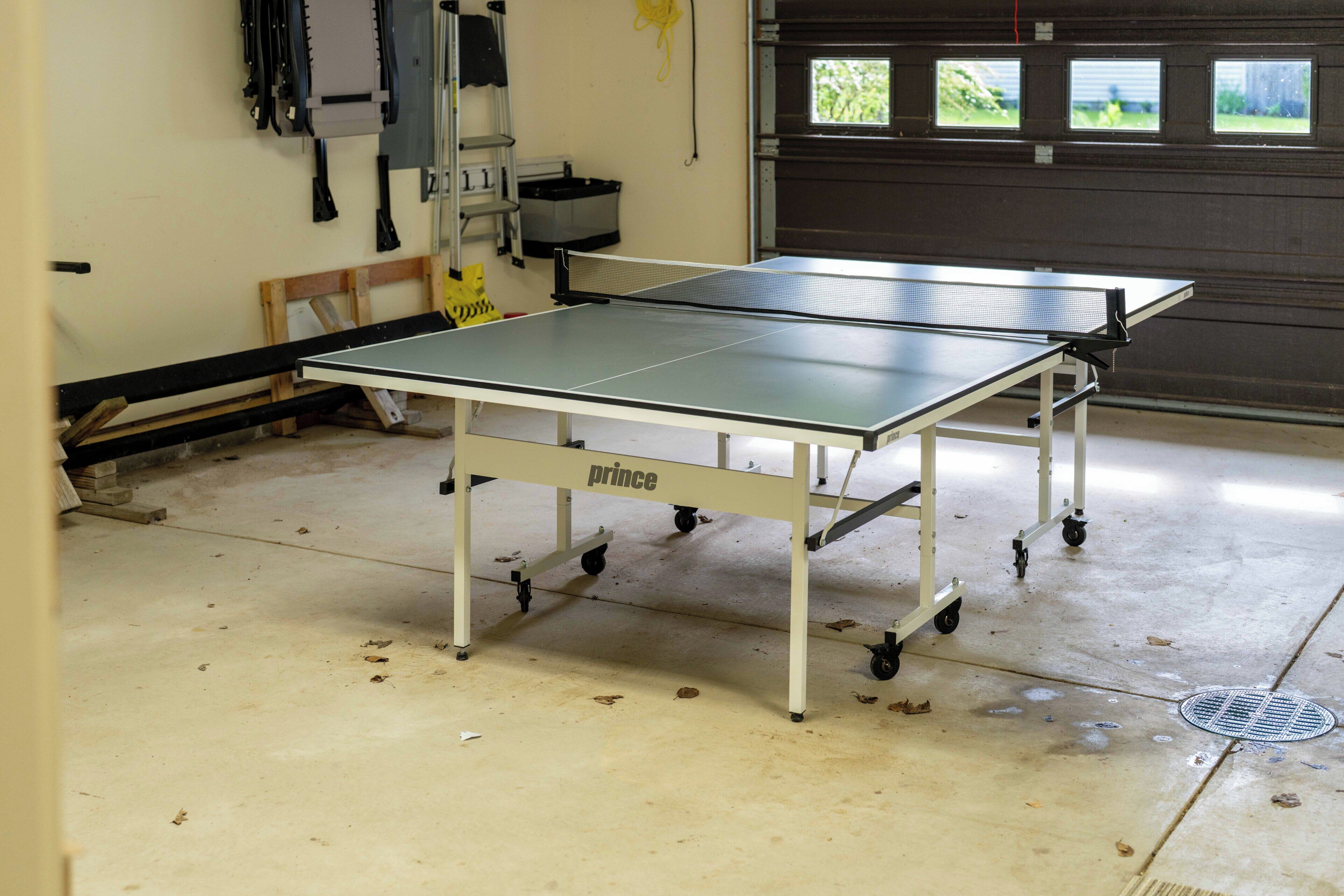 A portable ping pong table in a garage with a garage door in the background.