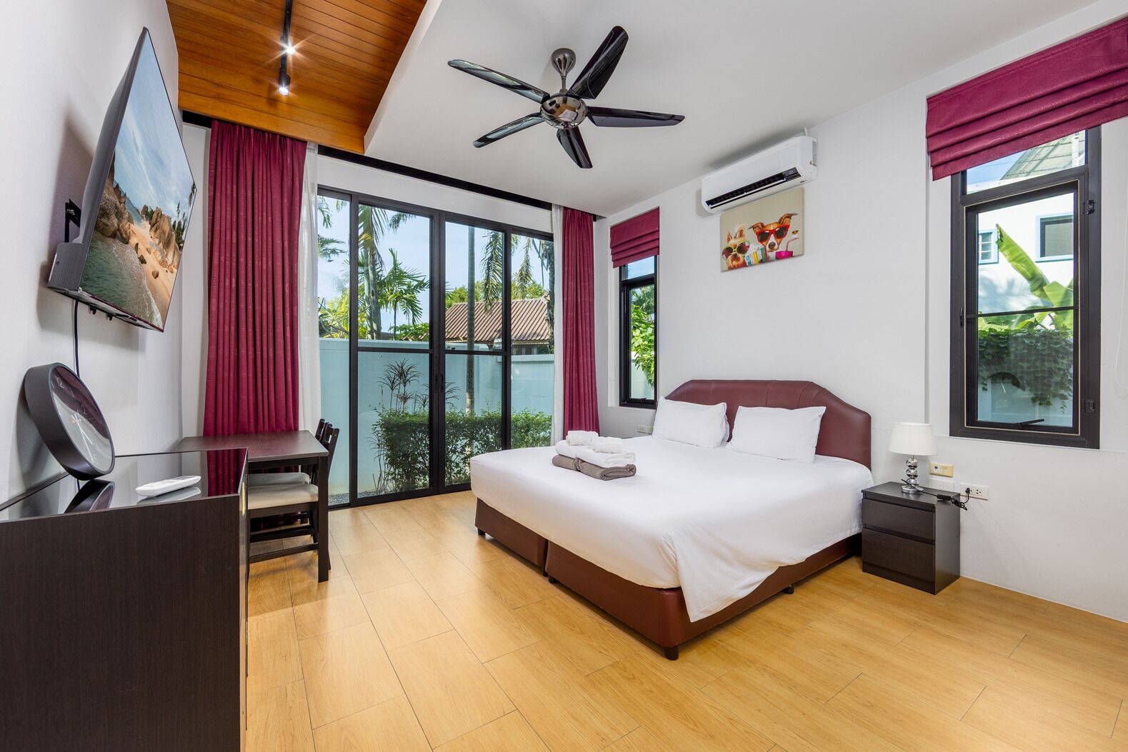 Ein modernes Hotelzimmer mit einem großen Bett, einem Schreibtisch, einem Sessel, einem Fernseher und einem Deckenventilator.