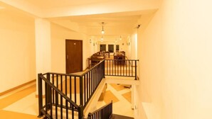 A hotel corridor with a staircase, a dining area with tables and chairs, and a wooden door at the end. - Eden Hill Hotel (Nuwara Eliya)