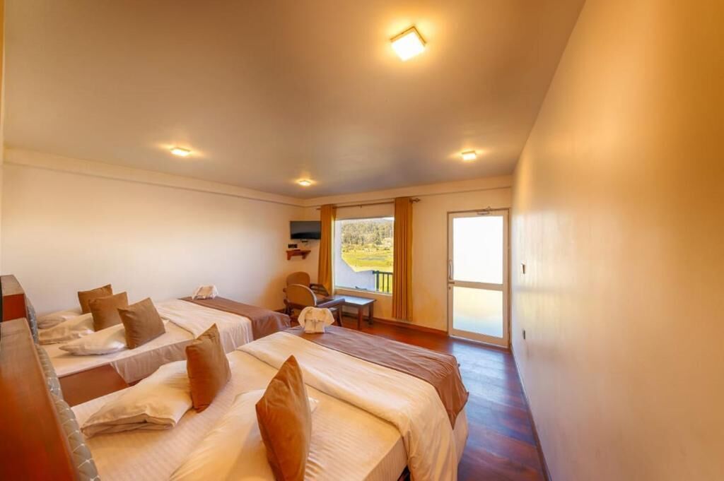 Ein Hotelzimmer mit zwei Betten, einem Schreibtisch und einem Sessel. Ein Fenster mit Vorhängen bietet einen Blick ins Freie.