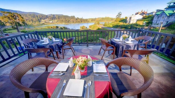 A terrace with tables set for dining, overlooking a lake and hills. - Eden Hill Hotel (Nuwara Eliya)