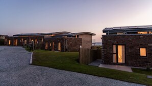A row of modern, stone-clad buildings with large windows and solar panels, set against a twilight sky.