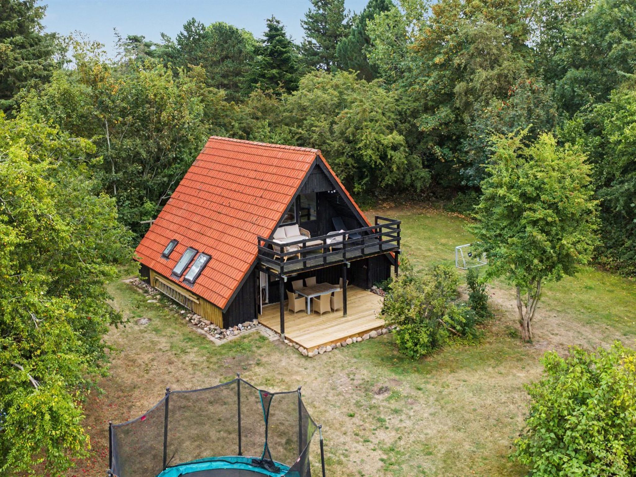 A cabin with a red roof, a deck, and a trampoline in the yard.