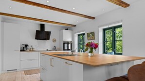 Cocina moderna con armarios blancos, encimera de madera y una isla grande. Se ve un ventanal con vistas a zonas verdes.