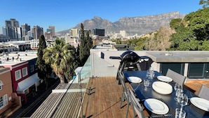 A rooftop terrace with a dining setup, overlooking a cityscape and mountains.