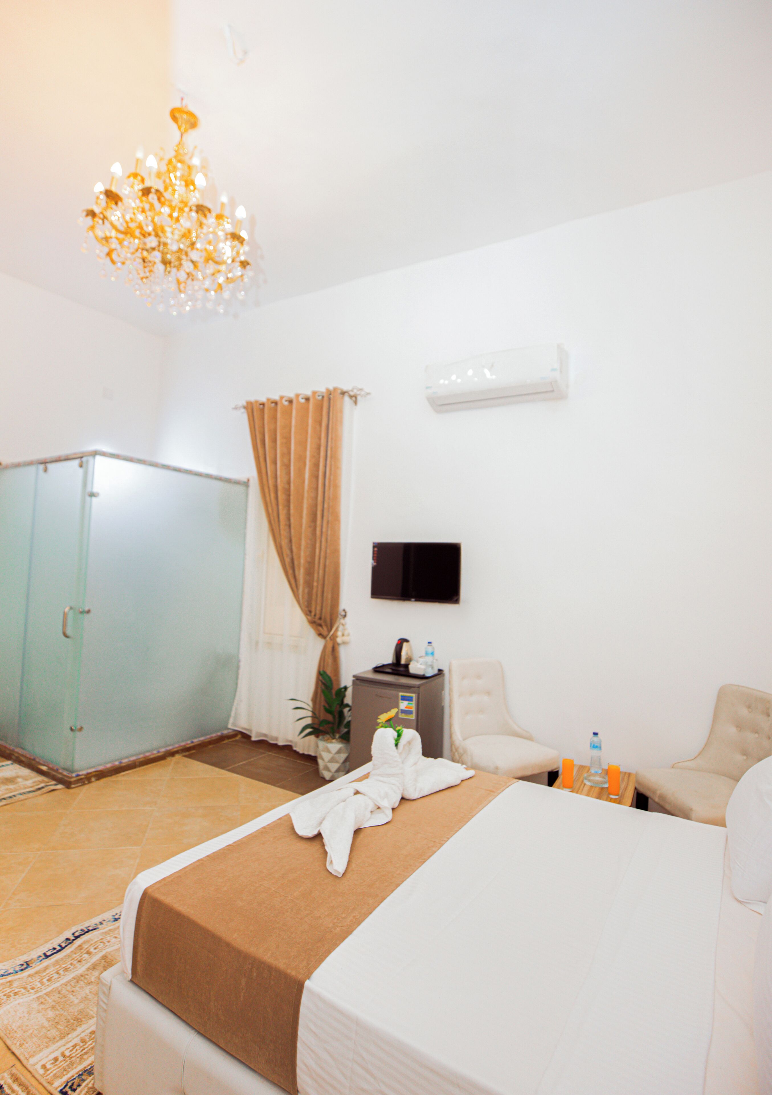 Quarto de hotel com cama, guarda-roupa, escrivaninha com cadeira, televisão e um candelabro.