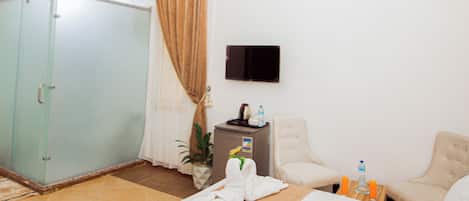 Quarto de hotel com cama, guarda-roupa, escrivaninha com cadeira, televisão e um candelabro.