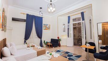 Habitación de hotel con dos camas, un sofá, una mesita y una silla. Cuenta con ventana con cortinas, un cuadro en la pared y un espejo.