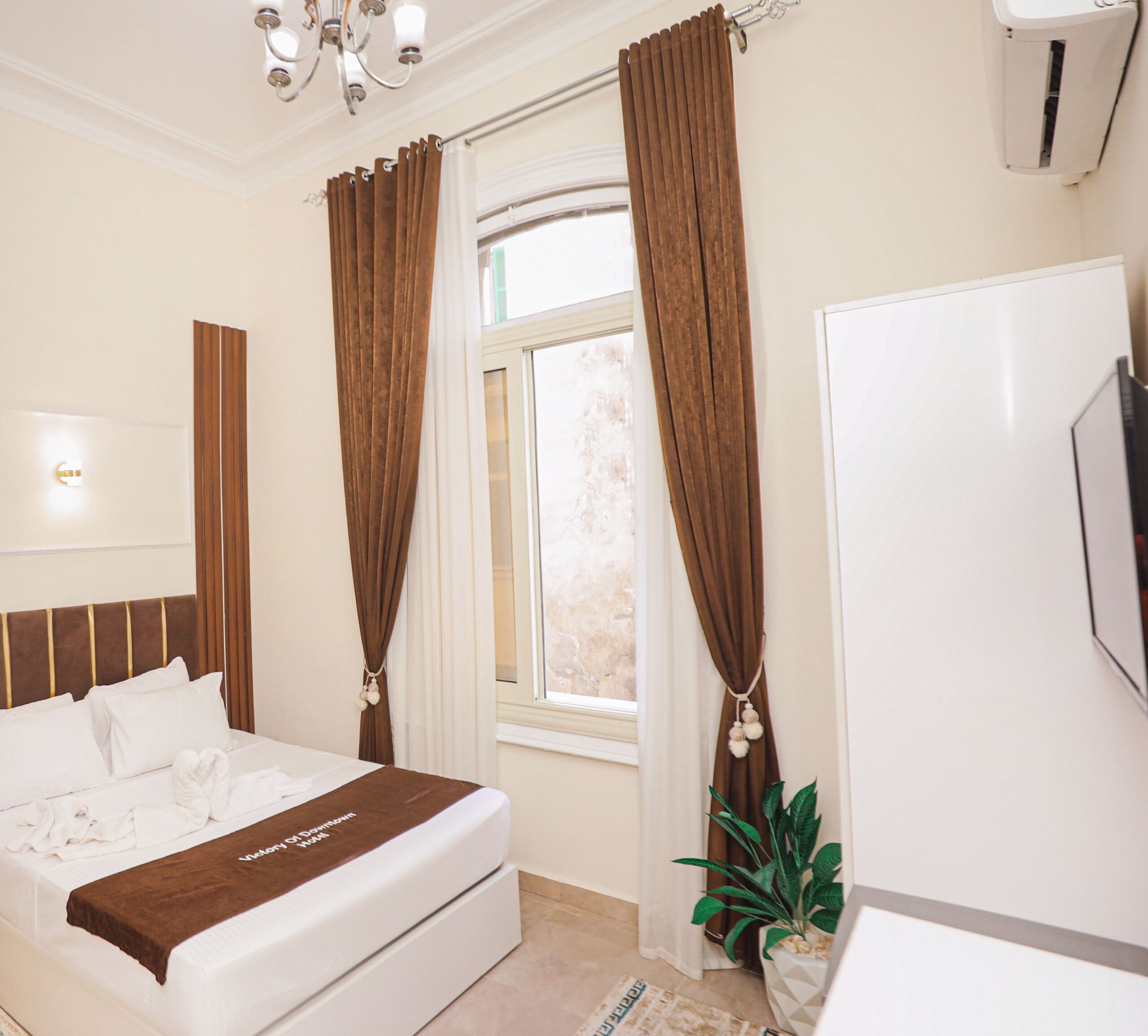 Ein Schlafzimmer mit Bett, Vorhängen, einer Pflanze und einem Fernseher.