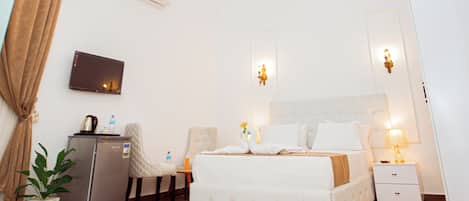 Ein Hotelzimmer mit Bett, Fernseher, Kühlschrank, Pflanze und einer Chandelier.