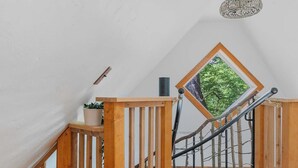 A loft bedroom with a wooden floor, a bed with a colorful blanket, a skylight, and a wooden staircase. - Whimsical Vermont Cabin | Hot Tub, Sauna & Views (Johnson)