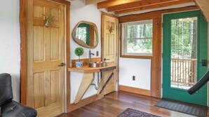 A wooden interior with a wooden door, a mirror, a sink, and a green door leading to a balcony. - Whimsical Vermont Cabin | Hot Tub, Sauna & Views (Johnson)