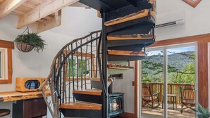 A spiral staircase with wooden steps and metal railings, leading to a deck with outdoor seating and a wood-burning stove. - Whimsical Vermont Cabin | Hot Tub, Sauna & Views (Johnson)