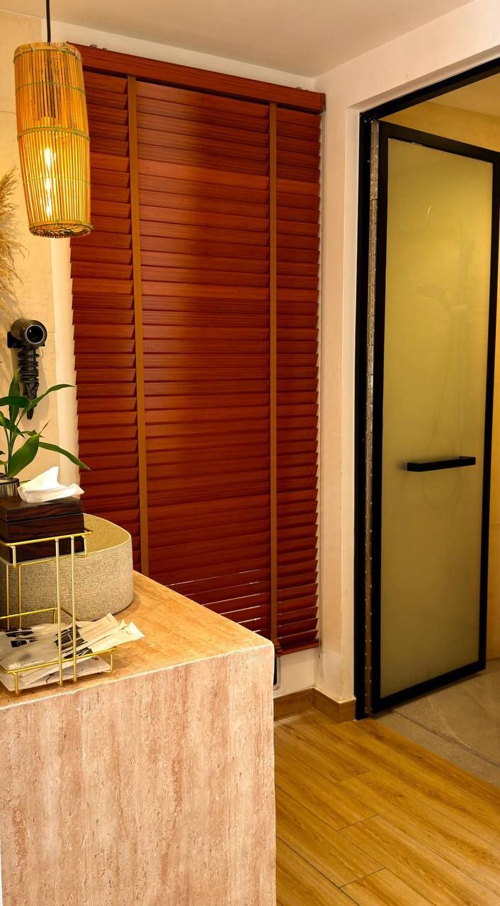 A room with a wooden floor, a concrete counter, a bamboo lamp, a wooden door, and a window with blinds.