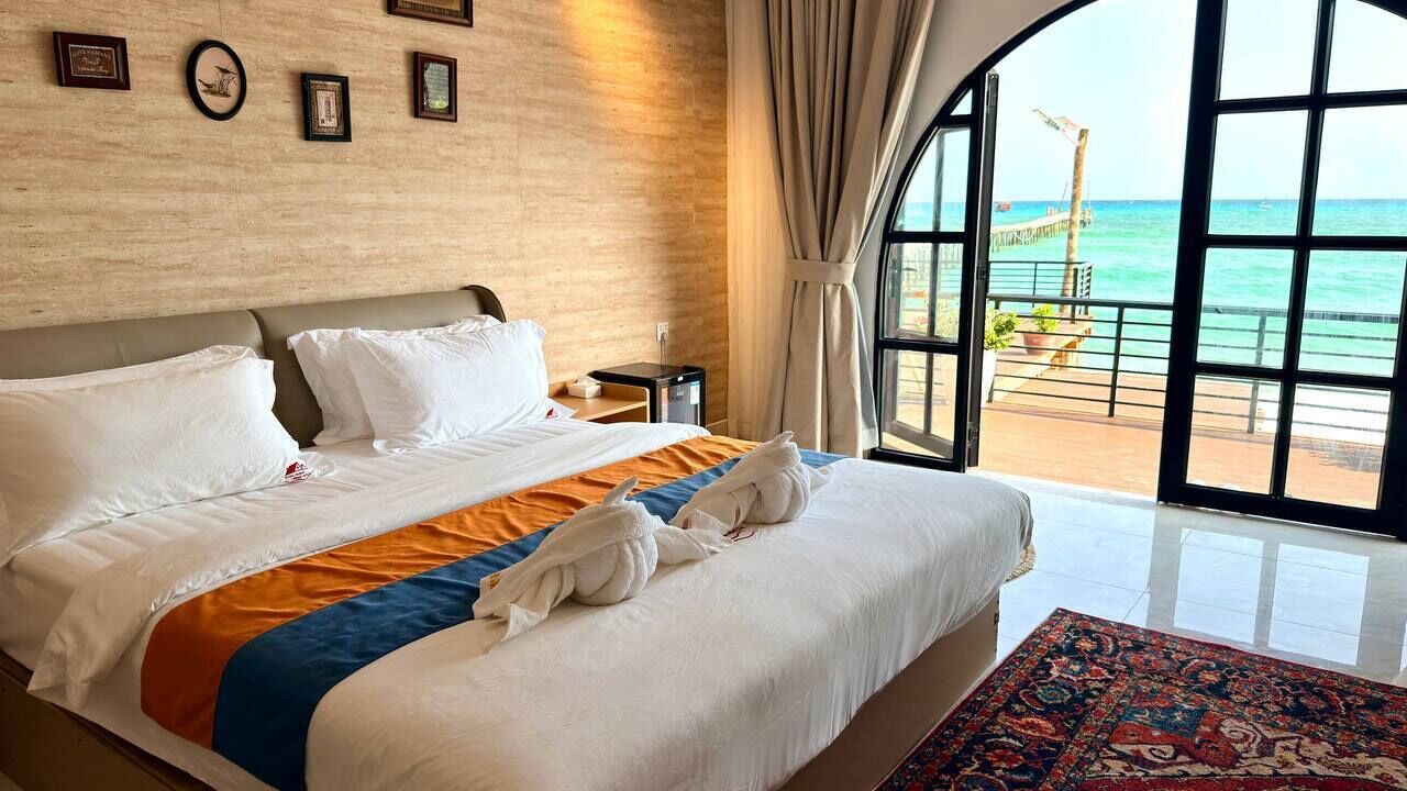 Habitación de hotel con una cama grande, vista al océano y un balcón con barandilla.