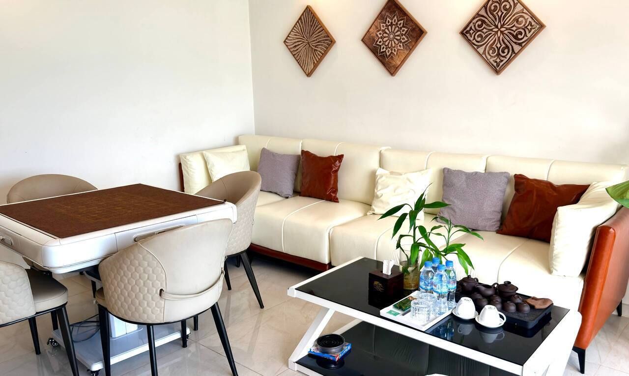 A modern living room with a white sofa, a glass coffee table, a dining table with chairs, and decorative wall art.