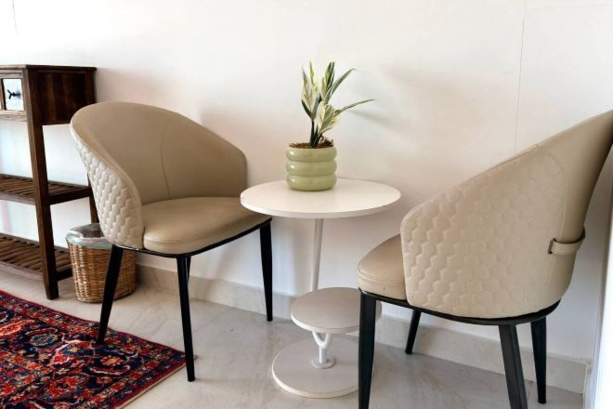 Two beige chairs with black legs, a small white table, and a potted plant.