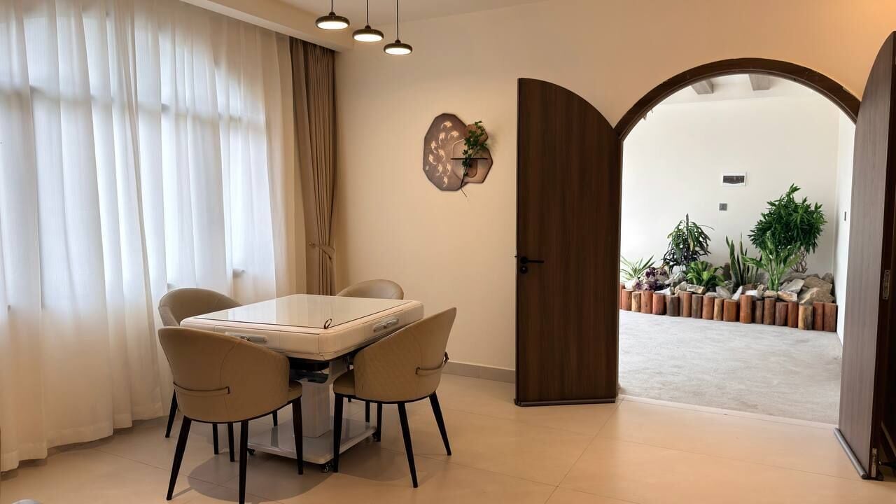 Un comedor con una mesa y sillas, un adorno en la pared, y un acceso a un jardín con plantas.