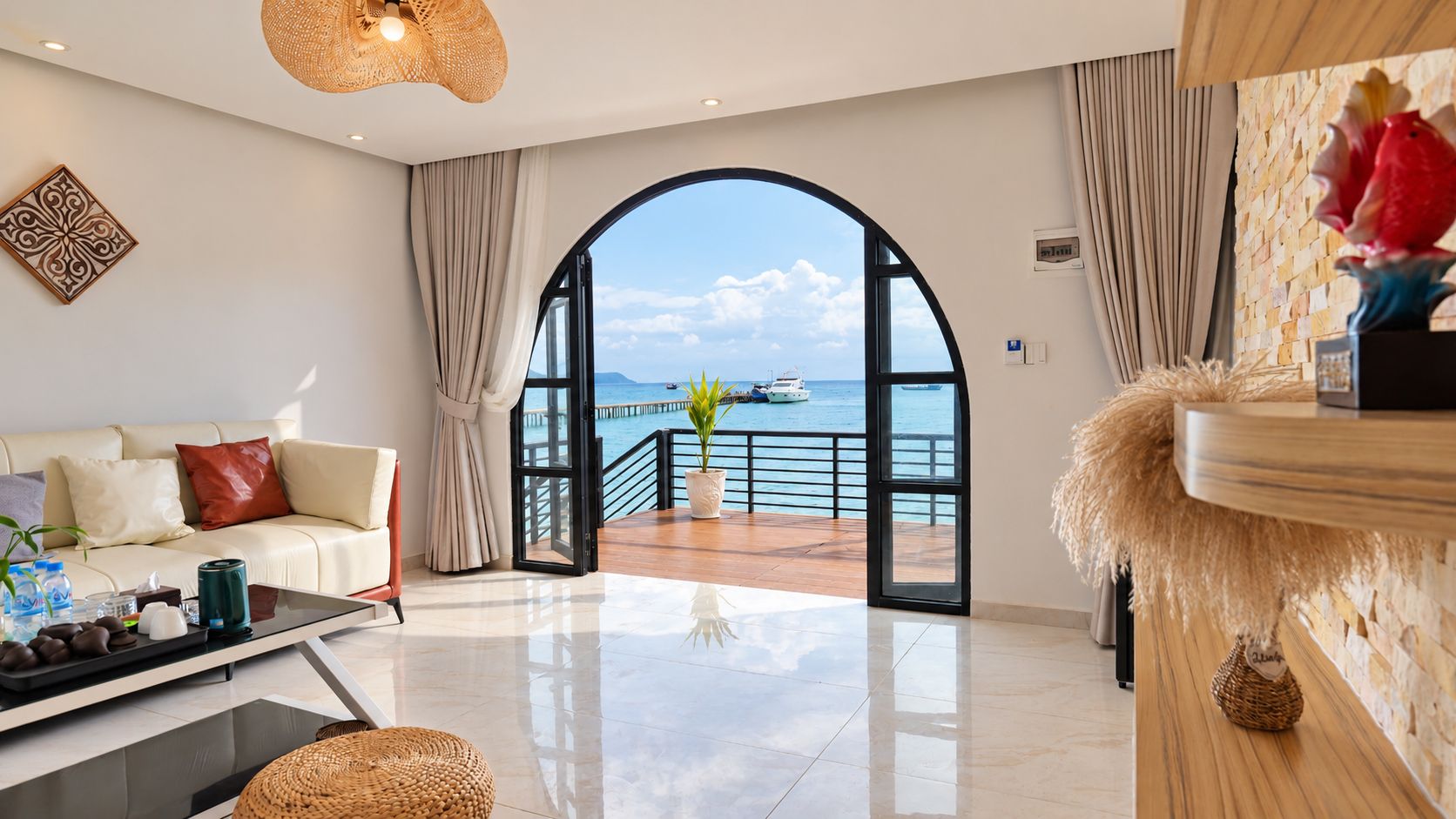 Un salón moderno con sofá, mesa de centro y vista al mar a través de un arco abierto.