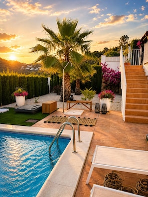 Ein Swimmingpool mit sonnigem Patio, einer Palme und einer Treppe, die zu einem Haus führt.